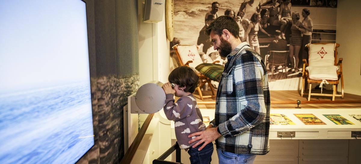Een vader en kind in een museumzaal, het kind tuurt door een verrekijker