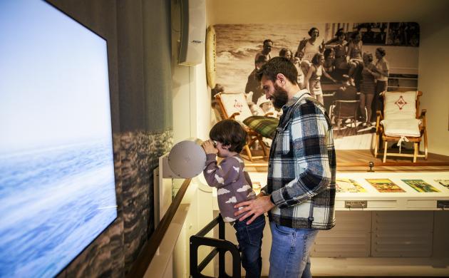 Een vader en kind in een museumzaal, het kind tuurt door een verrekijker