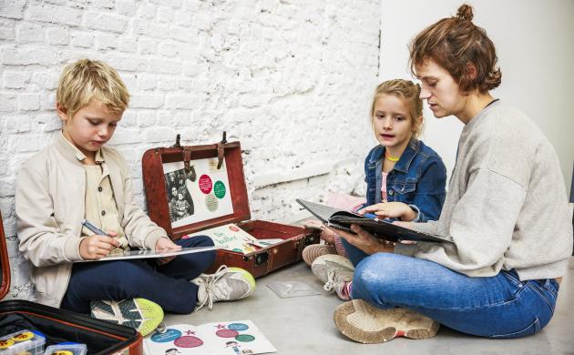 Een moeder zit met twee kinderen op de vloer en leest uit een boekje voor